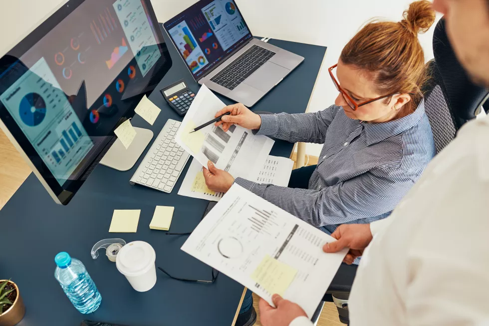 businesswoman-discussing-financial-data-with-colleague-sitting-desk-office-working-together